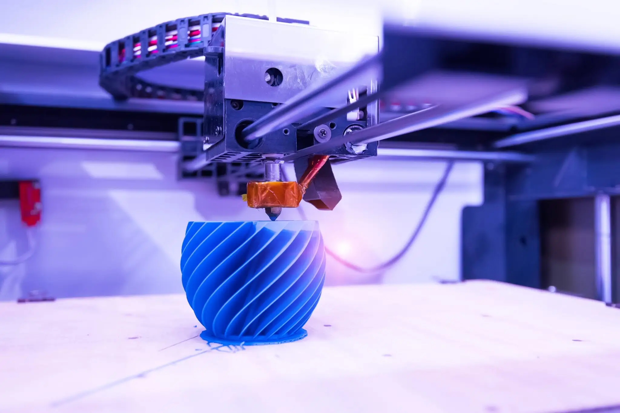 2.A 3D printer in operation, showcasing flexible prototyping by printing a blue, spiral-patterned object quickly on its build platform